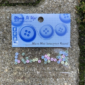 Könnte beinhalten: Eine Packung kleiner, runder Knöpfe in Pastellfarben. Die Knöpfe sind in den Farben Rosa, Blau und Grün gehalten. Die Packung ist mit "Micro Mini Innocence Round" beschriftet.