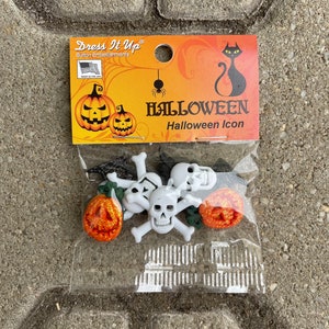 Puede incluir: Un paquete de botones con temática de Halloween con calaveras blancas con huesos cruzados y calabazas naranjas. El paquete está etiquetado como "Dress It Up" y "Halloween Icon".