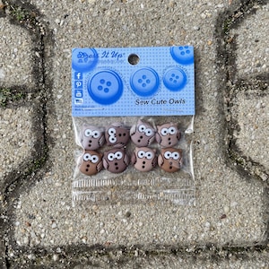 Könnte beinhalten: Eine Packung brauner Knöpfe in Form von Eulen mit weißen Augen. Die Packung ist mit "Sew Cute Owls" beschriftet und stammt von der Firma "Dress It Up".