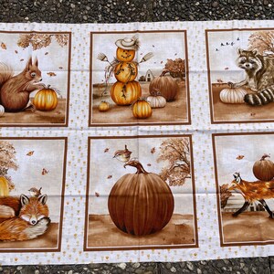 K&ouml;nnte beinhalten: Stoffpaneel mit sechs rechteckigen Szenen mit Herbstmotiven. Jede Szene hat einen braunen Rahmen und zeigt K&uuml;rbisse, Eichh&ouml;rnchen, Waschb&auml;ren, F&uuml;chse und eine Vogelscheuche. Der Hintergrund ist cremefarben mit einem kleinen, sich wiederholenden Muster.