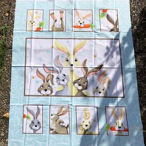 May include: A blue and white fabric panel with a repeating pattern of bunnies. The bunnies are in various poses, some holding carrots. The fabric is perfect for quilting, crafts, and home decor.