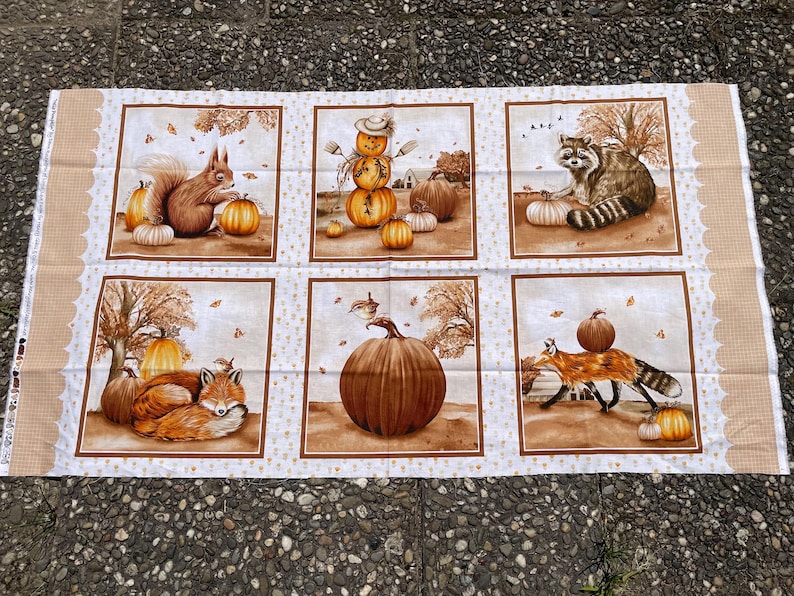 K&ouml;nnte beinhalten: Stoffpaneel mit sechs herbstlichen Szenen. Jedes Quadrat zeigt K&uuml;rbisse, Eichh&ouml;rnchen, Waschb&auml;ren, F&uuml;chse und eine Vogelscheuche. Die Farbpalette umfasst Braun-, Orange- und Cremet&ouml;ne und erzeugt eine gem&uuml;tliche Herbstatmosph&auml;re.