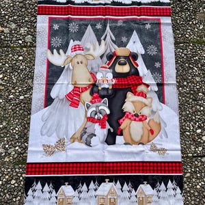 Peut inclure: Panneau de tissu rectangulaire avec une scène hivernale de dessins animés. Un orignal, un ours, un raton laveur et un renard portent des écharpes et des chapeaux. Le motif comprend des flocons de neige, des pins et des maisons, avec des bordures à carreaux rouges et noirs.