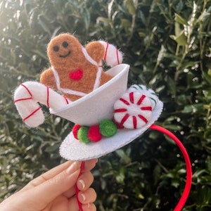 May include: A white felt headband with a gingerbread man, candy canes, and peppermint candies. The headband is red and white.