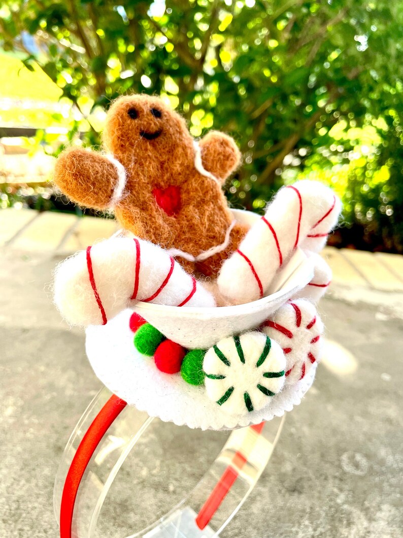 May include: A white headband with a gingerbread man, candy canes, and peppermint candies. The headband is red and white.