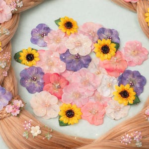 Puede incluir: Un peinado trenzado decorado con una variedad de accesorios florales para el cabello de colores. El arreglo incluye girasoles amarillos, flores rosas, moradas y blancas, creando un aspecto caprichoso. El cabello es de color castaño claro.