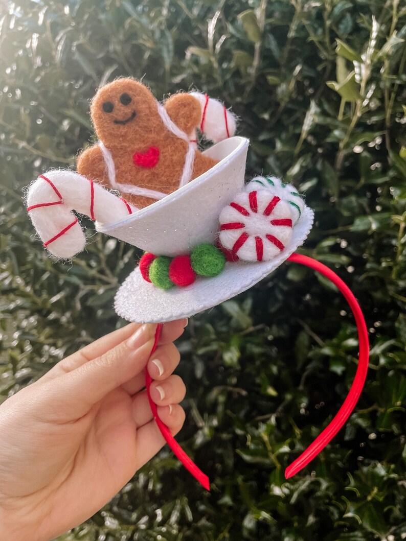 May include: A white felt headband with a gingerbread man, candy canes, and peppermint candies. The headband is red and white.