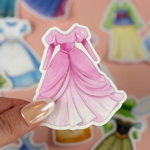 May include: A pink sticker of a princess gown with a full skirt and puffed sleeves. The dress is a light pink color with a white underskirt. Other sticker designs are visible in the background.