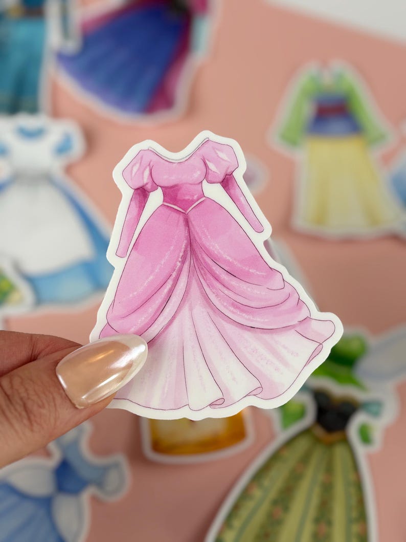 May include: A pink sticker of a princess gown with a full skirt and puffed sleeves. The dress is a light pink color with a white underskirt. Other sticker designs are visible in the background.
