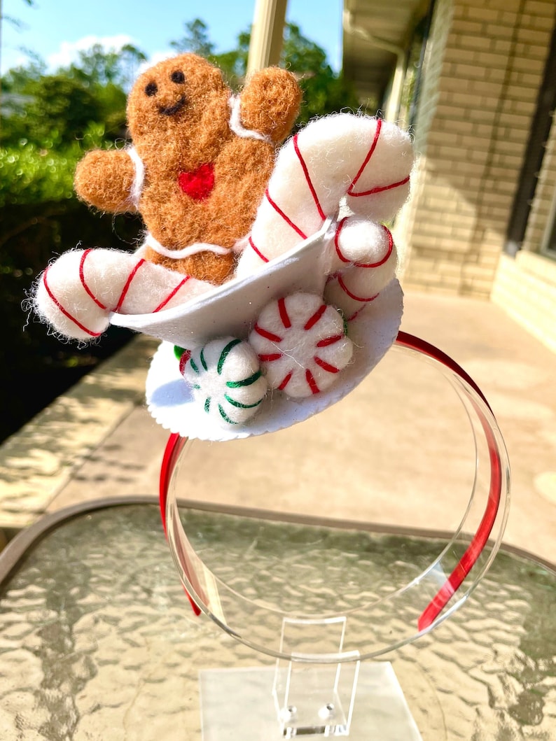 May include: A white headband with a felt gingerbread man, candy canes, and peppermint candies. The gingerbread man is wearing a red heart.