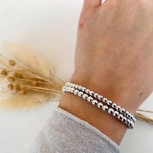 Könnte beinhalten: Ein silbernes Armband mit mehreren Reihen kleiner, runder Perlen. Das Armband wird am Handgelenk getragen.