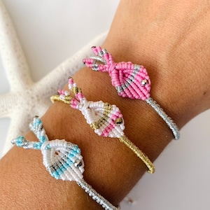 Peut inclure: Trois bracelets en macramé rose, blanc et bleu, avec des accents argentés et dorés. Les bracelets sont portés sur un poignet, mettant en valeur les nœuds complexes et les combinaisons de couleurs. Chaque bracelet a un design unique.