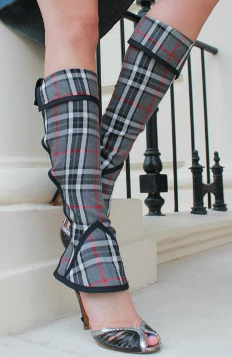 May include: A pair of grey and white tartan leg warmers with black trim. The leg warmers are worn with silver open-toe heels.