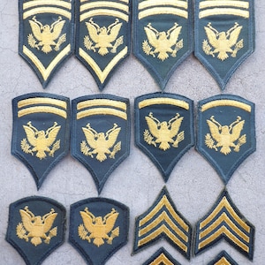 May include: A collection of vintage military patches. The patches are primarily navy blue with gold and yellow embroidered details. The designs include the American eagle and chevrons, indicating rank and service.