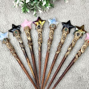 Puede incluir: Una colección de ocho palillos de pelo de madera, cada uno con una gema en forma de estrella en la parte superior. Las gemas son de varios colores, incluyendo rosa, negro y dorado. Los palillos tienen diseños tallados intrincados.
