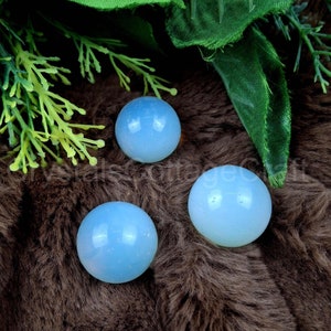 May include: Three smooth, round, light blue opal spheres on a brown fuzzy surface.