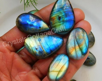May include: A collection of six iridescent labradorite gemstone cabochons in various shapes and sizes. The stones have a blue, green, and gold color with a shimmering effect.