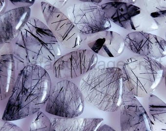 May include: A collection of clear quartz cabochons with black inclusions. The cabochons are various shapes and sizes, and have a translucent appearance.