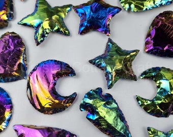 Op de afbeelding: Een verzameling van regenboogkleurige obsidianen pijlpunten, sterren en halve manen. De pijlpunten zijn in verschillende vormen en maten, en de sterren en manen zijn allemaal vijfpuntig. De obsidian is diep zwart met een regenboogkleurige glans.