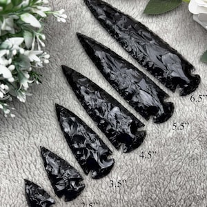 May include: A set of six black obsidian arrowheads of varying sizes, ranging from 1.5 inches to 6.5 inches. The arrowheads are arranged in a row from smallest to largest, with the text "Design-01" visible below the arrowheads.