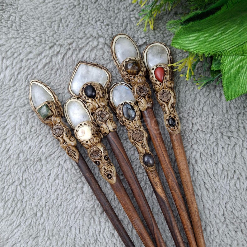 May include: Seven wooden hair sticks with carved details and gemstone accents. Each stick features a different gemstone, including a green stone, a black stone, a red stone, and a clear stone.