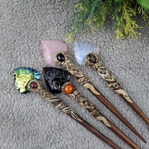 Puede incluir: Cuatro palos de pelo de madera con diferentes puntas de piedras preciosas. Los palos están decorados con intrincados tallados. Las piedras preciosas son rosa, azul, verde y negra.