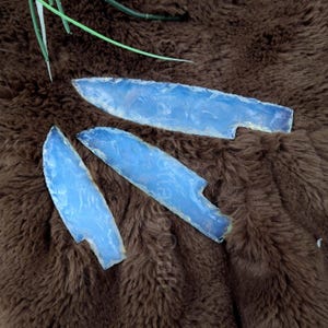 Könnte beinhalten: Drei blaue und weiße Achat-Messerklingen mit einer glatten, polierten Oberfläche. Die Klingen sind in Dreiecksform auf einer braunen, flauschigen Oberfläche angeordnet.
