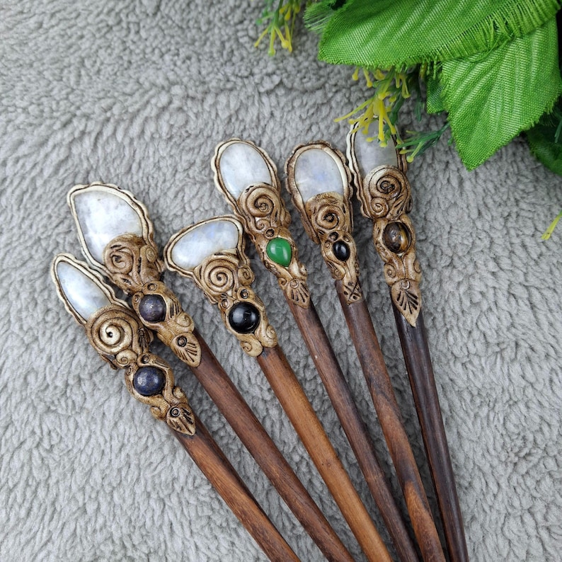 May include: Seven wooden hair sticks with moonstone tops and various colored gemstone accents. The sticks are brown and have intricate carvings.
