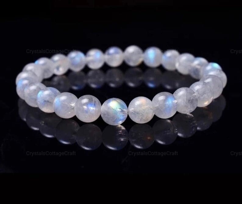 May include: A white moonstone bracelet with iridescent blue and green hues. The bracelet is made of round beads and is approximately 7 inches in length.