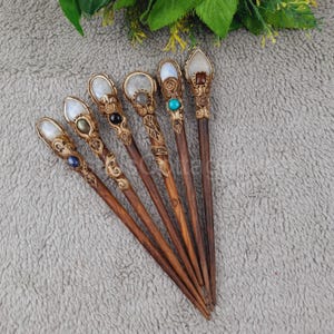 May include: Seven wooden hair sticks with decorative carvings and gemstone tops. The sticks are brown and the tops are adorned with various stones, including moonstone, turquoise, and onyx.