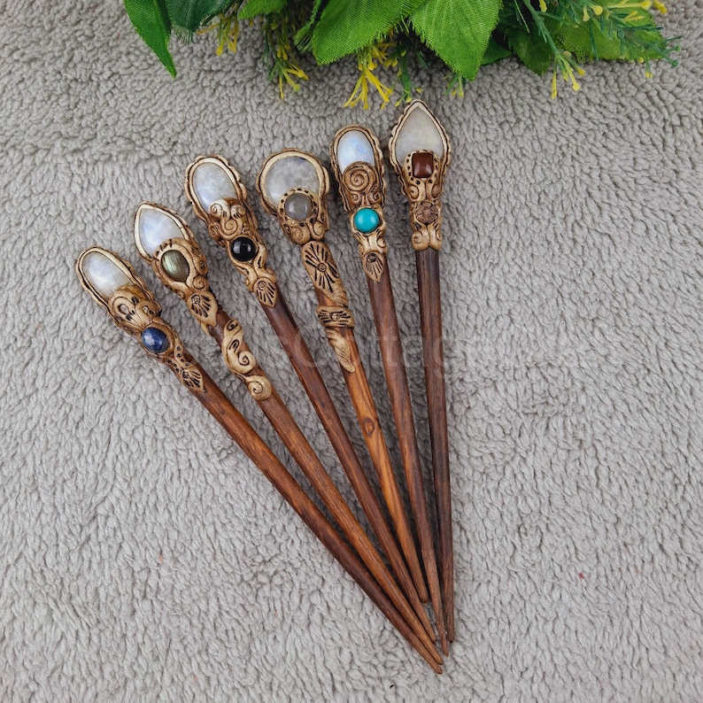 May include: Seven wooden hair sticks with decorative carvings and gemstone tops. The sticks are brown and the tops are adorned with various stones, including moonstone, turquoise, and onyx.