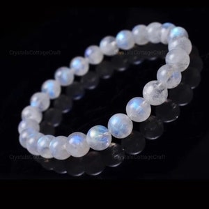 May include: A white moonstone bracelet with iridescent blue and white tones. The bracelet is made of round beads and is strung on an elastic cord.