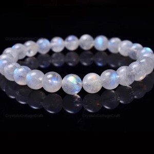 May include: A white moonstone bracelet with iridescent blue and green hues. The bracelet is made of round beads and is strung on elastic.
