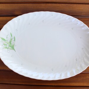 Könnte beinhalten: Weiße ovale Servierplatte mit einem grün-weißen Blumendesign. Die Platte hat einen erhöhten Rand und eine strukturierte Oberfläche.