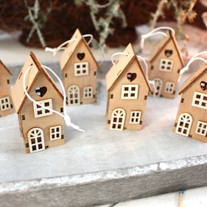 Könnte beinhalten: Sechs Holzhäuser mit weißer Schnur, jedes mit einem herzförmigen Ausschnitt und Fenstern, auf einem grauen Tablett angeordnet.