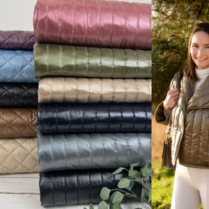 Può includere: Esposizione di giacche trapuntate in vari colori, tra cui viola, blu, nero e marrone. Le giacche presentano un motivo a rombi. Una donna indossa una giacca verde oliva abbinata. Le giacche sono realizzate in materiale lucido.