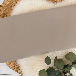 May include: A close-up of a light brown fabric swatch. The fabric is smooth and has a subtle sheen. It is displayed on a white faux fur rug.