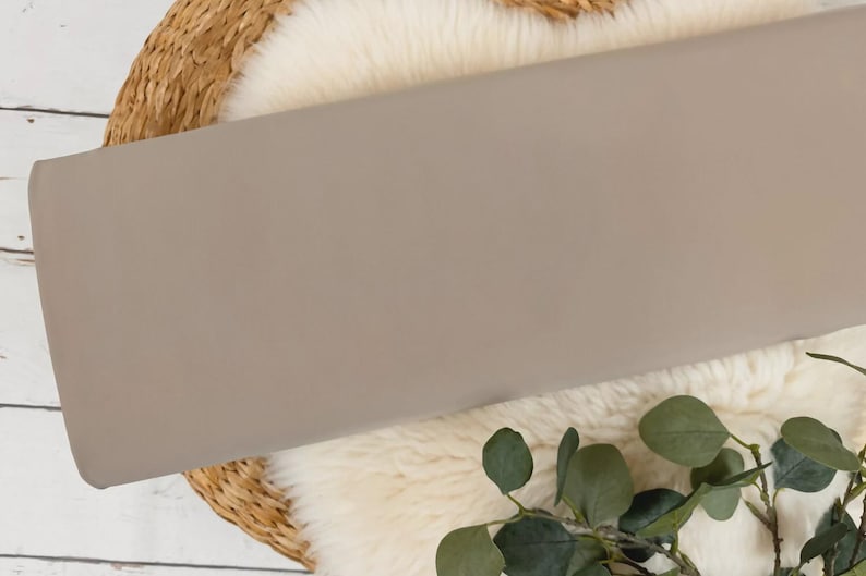 May include: A close-up of a light brown fabric swatch. The fabric is smooth and has a subtle sheen. It is displayed on a white faux fur rug.