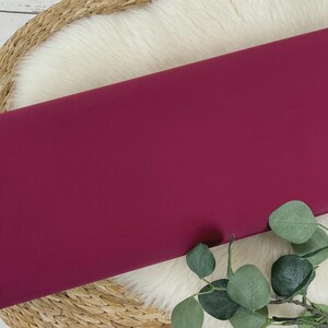 May include: A solid, deep burgundy fabric swatch. The fabric is smooth and has a slight sheen.