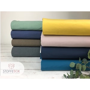 Könnte beinhalten: Ein Stapel aus sechs verschiedenen Stoffproben in unterschiedlichen Farben. Die Proben sind von oben nach unten in folgender Reihenfolge angeordnet: Gelb, Rosa, Braun, Dunkelblau, Türkis und Grün. Die Proben sind alle gleich groß und in der Mitte gefaltet. Der Stoff ist ein weicher, dehnbare Strick.