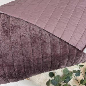 May include: A soft, plush throw blanket in a mauve color with a quilted, mauve-colored backing. The blanket is folded in half and the backing is visible.