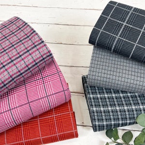 Puede incluir: Muestras de tela con varios diseños de cuadros. Las telas presentan colores como rosa, rojo, gris y negro. Las muestras están dispuestas sobre una superficie de madera clara.