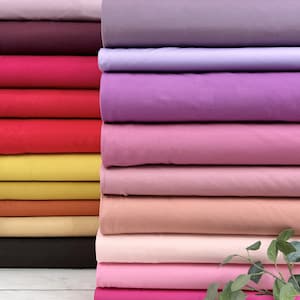 Puede incluir: Una pila de muestras de tela de colores en varios tonos de rosa, morado, rojo, naranja, amarillo y marr&oacute;n. La tela es lisa y parece ser de algod&oacute;n.