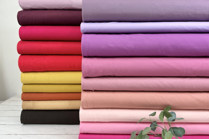 Puede incluir: Una pila de muestras de tela de colores en varios tonos de rosa, morado, rojo, naranja, amarillo y marr&oacute;n. La tela es lisa y parece ser de algod&oacute;n.
