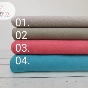 Op de afbeelding: Vier rollen stof in verschillende kleuren: lichtgrijs, olijfgroen, koraalroze en turquoise. De rollen zijn genummerd van 01 tot 04. Het STOFFEBOX-logo is zichtbaar. Perfect voor doe-het-zelf projecten.