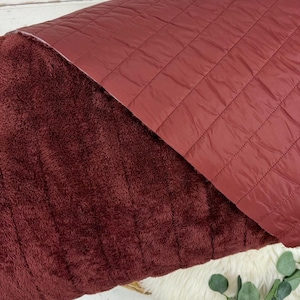 May include: A burgundy quilted blanket with a soft, plush side. The blanket is folded in half, showing both sides of the fabric.