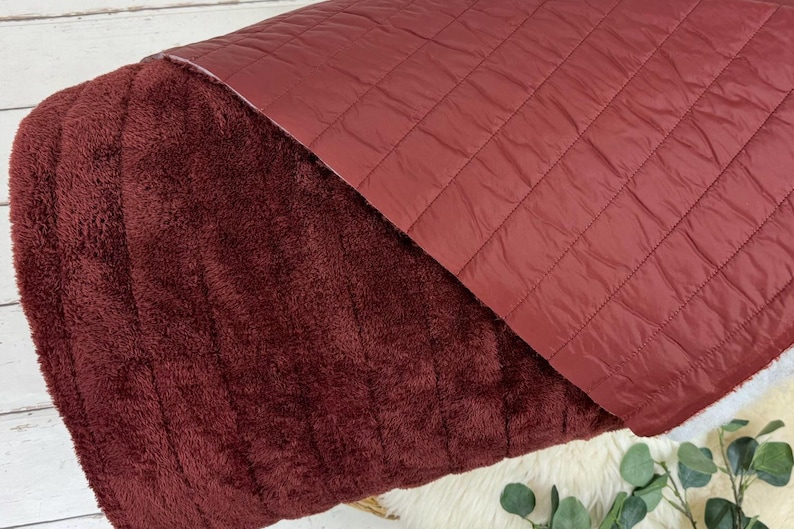 May include: A burgundy quilted blanket with a soft, plush side. The blanket is folded in half, showing both sides of the fabric.