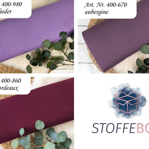 Puede incluir: Tres muestras de tela en diferentes tonos de morado. La muestra superior es de color morado claro y est&aacute; etiquetada como "Art. Nr. 400-980 dunkel flieder". La muestra del medio es de color morado oscuro y est&aacute; etiquetada como "Art. Nr. 400-670 aubergine". La muestra inferior es de color burdeos oscuro y est&aacute; etiquetada como "Art. Nr. 400-860 dunkel bordeaux". Las muestras se muestran sobre una superficie blanca con una base de madera y hojas verdes.