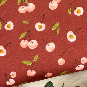 May include: A red fabric with a repeating pattern of pink cherries with green stems and leaves.