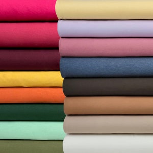Op de afbeelding: Een stapel van 10 verschillende gekleurde stofstalen. De kleuren zijn: roze, rood, bordeauxrood, geel, oranje, groen, lichtgroen, olijfgroen, beige en wit.